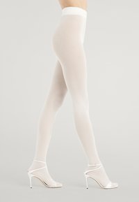 Calze bianche a coste con vita alta, abbinate a sandali bianchi con tacco alto caratterizzati da una sottile fascia e una punta appuntita.