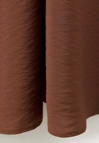 Rideau en tissu marron foncé suspendu avec une texture visible et une couture le long du bord inférieur sur un fond neutre.
