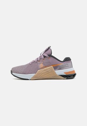Chaussure de sport basse violette avec tissu texturé, accent orange et semelle intermédiaire beige angulaire, vue de côté extérieur sur fond blanc.