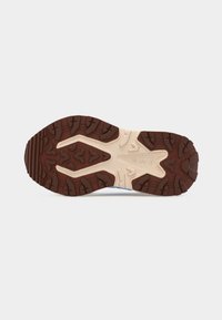 Potplat cipele s grubim smeđim i bež uzorkom gaznoga sloja dizajniranim za prianjanje na otvorenom na svijetlosivoj pozadini.