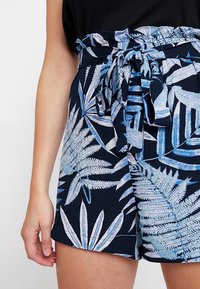 Granatowe szorty z kwiecistym wzorem farnym w jasnoniebieskim kolorze, z elastycznym pasem w talii i związanym paskiem z materiału, umożliwiającym regulację dopasowania.