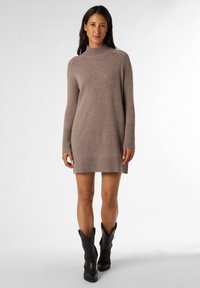 Strickkleid in hellem Taupe mit hohem Kragen, langen Ärmeln, gerippten Bündchen und weichem Material, kombiniert mit schwarzen Cowboystiefeln.