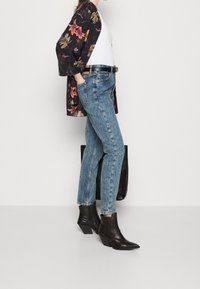 Černý květinový kimono, bílý top bez rukávů, modré rovné džíny a černé špičaté kotníkové boty. Obsahuje hnědý opasek a černou tašku na rameno.