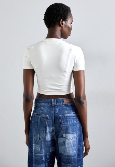 White cropped t-shirt with short sleeves, paired with blue denim pants featuring a newspaper print and multiple pockets.