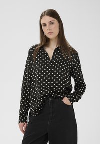 Fekete, fehér pöttyös, gombos ing, gallérral és hosszú ujjakkal. Magas derekú sötét farmerral viselve, lazább szabással.