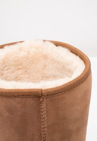 Primer plano de la parte superior de una bota de ante marrón forrada con suave y esponjosa lana de oveja de color crema.