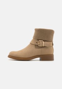 Beige ankelstøvler med ribbestrikket mansjett, semsket utseende, detalj med sidebuckle, og en lav firkantet hæl.