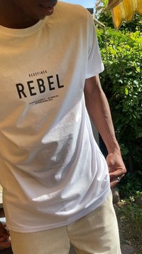 Biała bawełniana koszulka z czarnym nadrukiem graficznym z napisem "REBEL". Klasyczny dekolt; dopasowany krój z krótkimi rękawami.