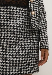 Black and white houndstooth patterned fabric with a textured finish, featuring a pearl-button closure at the collar and a tailored fit.
