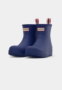 Bocanci de cauciuc bleumarin, de tip ankle, cu vârf rotund, talpă cu textură pentru aderență și mânere în dungi roșii și albe cu etichete "HUNTER".