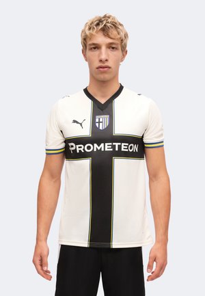 Jeune homme portant un maillot de football blanc avec une croix noire, des bordures bleues et jaunes, le logo de Parma Calcio et le texte du sponsor Prometeon.