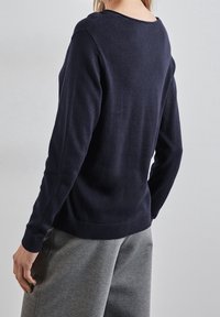 Mörkblå långärmad tröja i mjukt stickat material med rundad halsringning och ribbat nederkant, bärs tillsammans med gråa sweatpants.