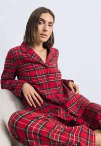 Rød ternet pyjamas sæt lavet af blødt flannel. Indeholder en knaplukket skjorte og løstsiddende bukser med krave, der viser et klassisk tartanmønster.