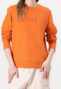 Orange long-sleeve sweatshirt with ribbed cuffs and crew neck. Features a faded "BOSS" logo on the front. Soft, textured fabric.