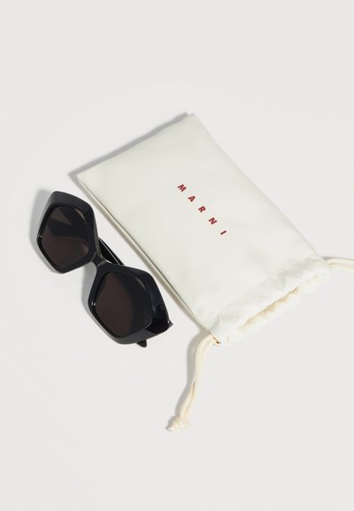 Black oversized hexagonal sunglasses next to a white drawstring pouch with "MARNI" printed in red letters.