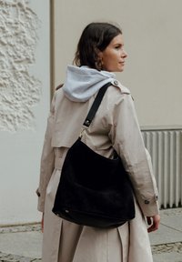 Black suede shoulder bag with a soft, curved shape and minimalistic design, featuring a black strap and subtle metallic hardware accents.
