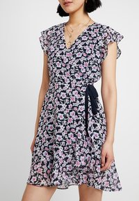 Blommig klänning i marinblått med rosa och vita blommor, korta volangärmar, V-ringning, knytlinning i midjan och lätt, genomskinligt tyg.