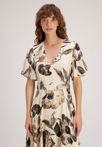 Blumenkleid in creme- und Brauntönen, mit kurzen, schwingenden Ärmeln, einem tiefen V-Ausschnitt und einer taillierten Taille, die in einen fließenden Rock übergeht.