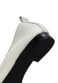 Zapato plano de cuero blanco con punta redondeada y suela de goma negra. Presenta una superficie texturada y un sutil detalle de costura en el borde.