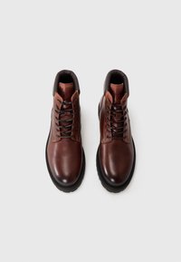 Botas de tobillo de cuero marrón con punta redonda, suela de goma negra y un cuello de imitación de cuero marrón en contraste con cordones. Diseñadas para la durabilidad.