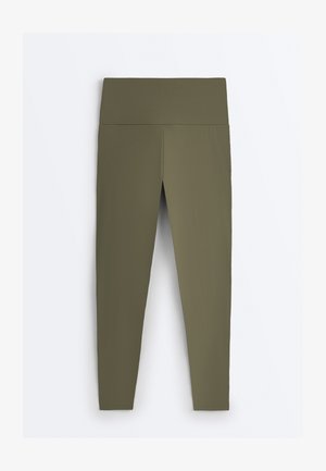 Bezšvové legíny olivovo zelenej farby s vysokým pásom a širokým pásikom, položené na bielom pozadí.