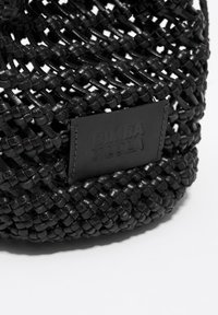 Zbliżenie na czarną plecioną skórzaną torbę z naszywką w kształcie prostokąta z przeszyciami, embossowaną napisem "BIMBA Y LOLA".