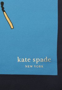 Sfondo in tessuto blu con un grafico di un fiammifero, testo dorato "kate spade NEW YORK" e una sezione contrastante di colore blu scuro.