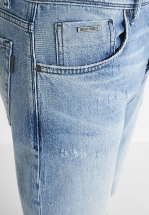 Jeans in denim azzurro chiaro con una vestibilità slim, caratterizzati da leggere scoloriture, una tasca posteriore con etichetta e dettagli in metallo scuro.