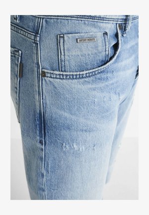 Hellblaue Denim-Jeans im Slim-Fit, mit leichten Used-Effekten, einer Gesäßtasche mit Etikett und dunklen Metallakzenten.