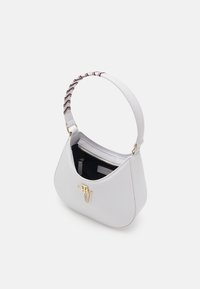 Biała skórzana torebka o zakrzywionym kształcie, z akcentem w postaci złotego metalowego okucia oraz wzorzystym paskiem w czerwono-czarną kratę. Wewnątrz znajduje się kieszeń na zamek.