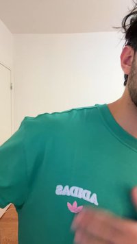 Žalia medvilninė marškinėlė su apvalia iškirpte, dekoruota baltu užrašu „ADIDAS“ ir rožiniu trefoil logotipu. Lygi tekstūra, laisvo stiliaus prigludimas.