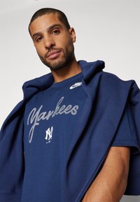 Camiseta navy con "Yankees" en una escritura plateada, logo de Nike en el pecho y un emblema blanco que contrasta. Material suave de algodón con mangas cortas.
