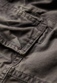 Tissu gris avec des coutures et des plis visibles. Présente une poche et des textures variées sur la surface, mettant en avant un design décontracté.
