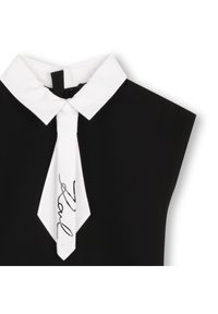 Top negru cu guler și cravată albă, decorat cu un grafic semnătură. Material neted, design structurat și mâneci scurte.