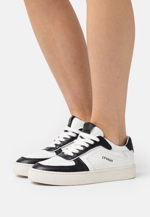 Bílé a černé kožené tenisky s texturovaným povrchem, zdobené perforovanými prvky, plochými tkaničkami a bílou gumovou podrážkou. Logo na straně.