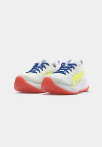 Baskets de course avec une tige en mesh blanc, des lacets bleus, des accents jaunes fluo et une semelle rouge vif. Conçues pour le confort et le soutien.