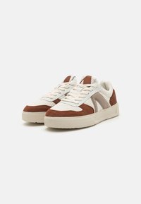 Sneaker mit einem strukturierten Obermaterial aus beiger und brauner Wildleder, weißen Mesh-Details und einer dicken, cremefarbenen Gummisohle mit einem geometrischen Muster.