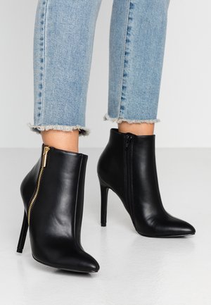 Bottines en cuir noir avec un bout pointu et des talons aiguilles. Présentent des zips latéraux avec des accents dorés et une texture lisse.