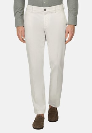 Uomo che indossa pantaloni bianchi su misura con tasche laterali, vita abbottonata, abbinati a una camicia grigia e mocassini in camoscio marroni.