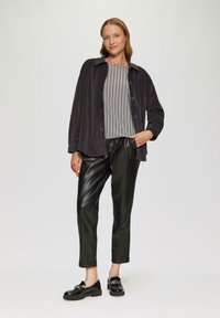 Donkergrijze corduroy jacket met knopen, gestreepte zwart-witte top, zwarte faux lederen broek en zwarte instappers met een gesp.