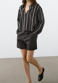 Black and white long-sleeve shirt with vertical stitching pattern, paired with black shorts and black slip-on shoes. Smooth, textured fabric.