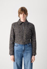 Giacca corta in tweed bianco e nero con chiusura a zip, colletto arrotondato e spalle strutturate, abbinata a denim azzurro chiaro.