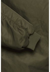 Manche de veste bomber vert olive avec poignet élastique et tissu froncé. Matériau lisse et léger avec un subtil éclat et une finition mate.