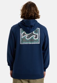 Sudadera azul marino con un patrón abstracto colorido y borde blanco en la parte posterior. Hecha de una tela suave con capucha ajustable y puños acanalados.