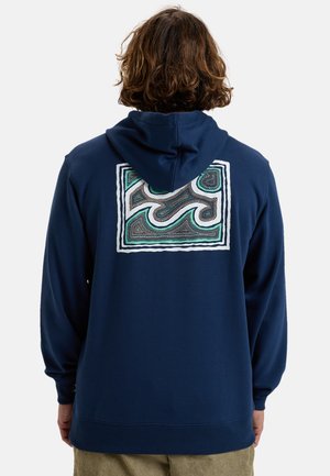 Hoodie bleu marine avec un motif abstrait coloré bordé de blanc au dos. Fabriqué en tissu doux avec une capuche à cordon et des poignets côtelés.