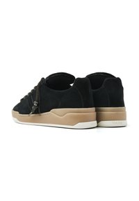 Black suede sneakers with a beige rubber sole, featuring a distinctive lacing system and textured accents on the heel.
