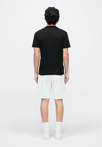 Czarny t-shirt z krótkim rękawem, bawełniana tkanina, w połączeniu z białymi szortami dresowymi. Dopełnieniem stroju są białe skarpetki i trampki. Widok od tyłu.