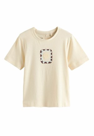 T-shirt à manches courtes couleur crème avec un motif central de coquillage encadré par un carré bleu et marron à motifs.