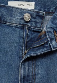 Jeans de denim azul con cremallera, cierre de botón y detalles de costura en tono claro. La tela tiene una ligera textura deslavada.