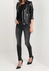 Chaqueta de cuero negra con bolsillos con cremallera, top negro ajustado, jeans ajustados de mezclilla oscuros y tacones altos negros con punta. Textura suave en todo.